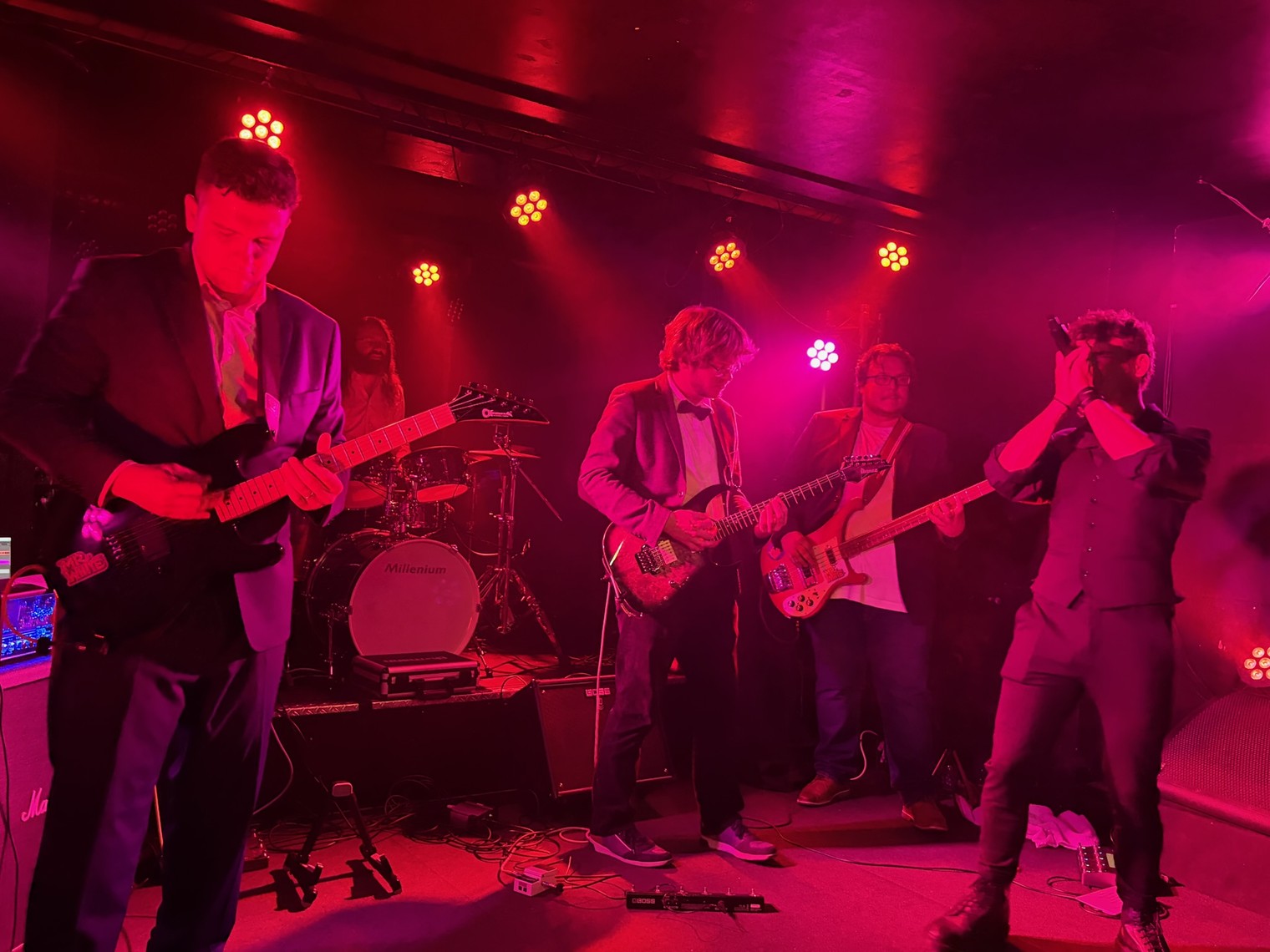 A band performing live on a small club stage under red stage lights