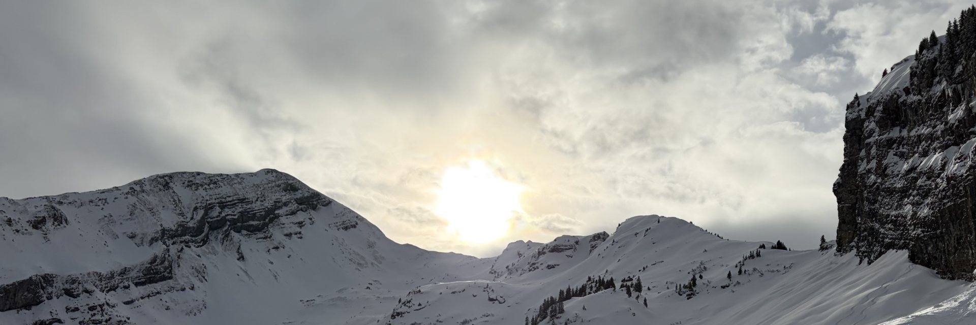 Sun breaking through clouds over snow-covered mountains